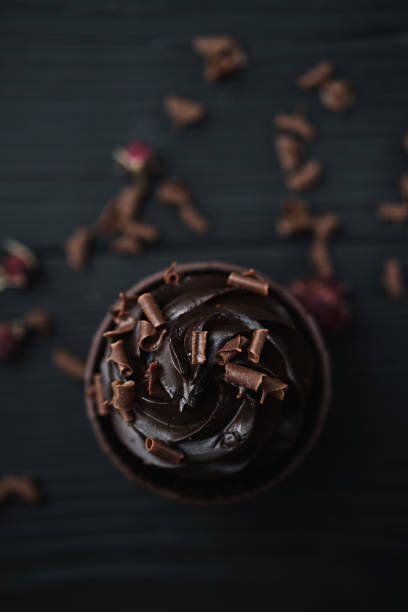 istock Muffin or cupcake with chocolate shaped cream at black table. Flatlay top view. 1297975260