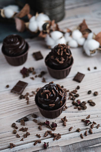 istock Several muffins or cupcakes with chocolate shaped cream at white table. Festive candle burns on a chocolate cake. There are chocolate chips scattered nearby. 1297975270