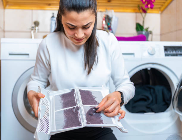 Young woman is removing lint from fluff dust filter of the tumble dryer. Dust and dirt trapped by the clothes dryer filter. Laundry processes Young woman is removing lint from fluff dust filter of the tumble dryer. Dust and dirt trapped by the clothes dryer filter. Laundry processes dryer stock pictures, royalty-free photos & images