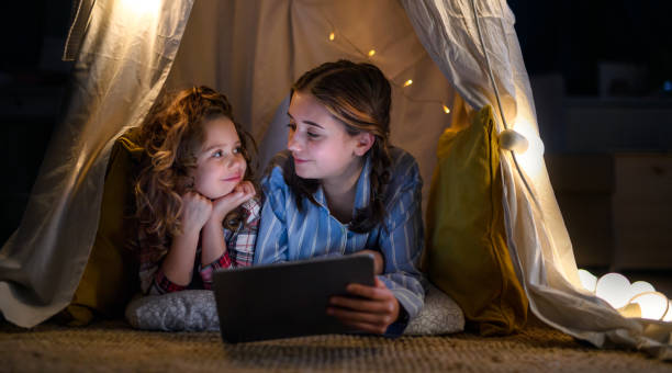 istock Sisters indoors at home, using tablet in pajamas. Lockdown concept. 1297978808