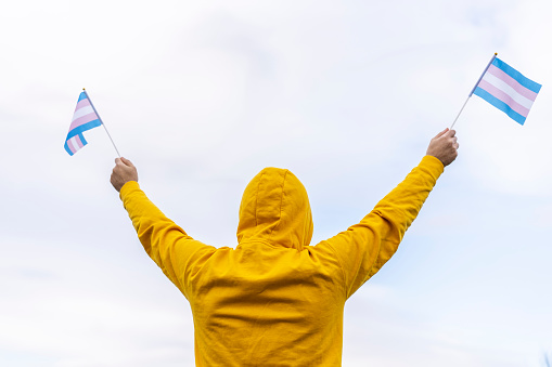 Young woman with dark brown hair on lightblue background wearing blue and yellow flag of Ukraine. Girl is smiling holding fingers crossed as a sign of victory, world peace.