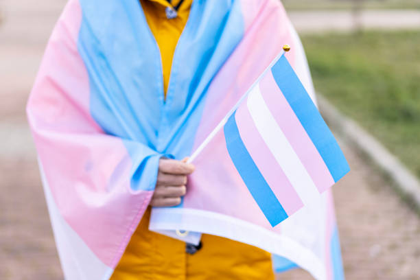 Transgender woman covered with the transgender flag and holding a flag in the hand for defending her rights