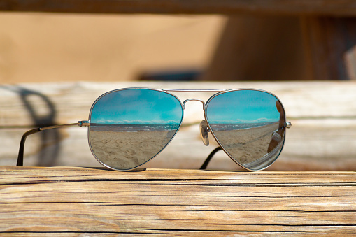 Fashion sunglasses on the wooden table. Sea reflection. Travel and vacation concept