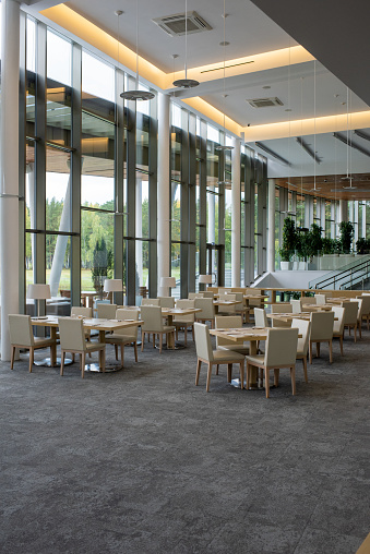 Interior of five star restaurant inside contemporary business center with many tables surrounded by chairs standing along big windows