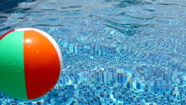 Beach ball in pool. Colorful inflatable ball floating in swimming pool.