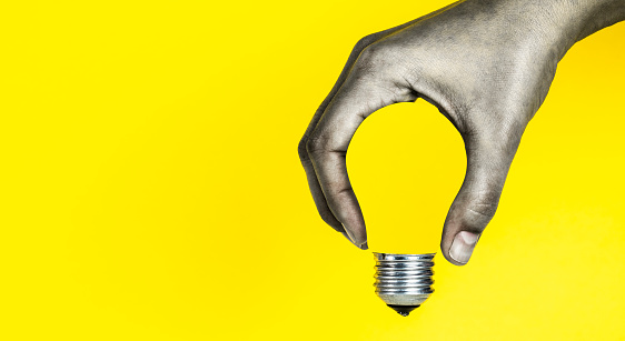 Light bulb in human hand, yellow background.