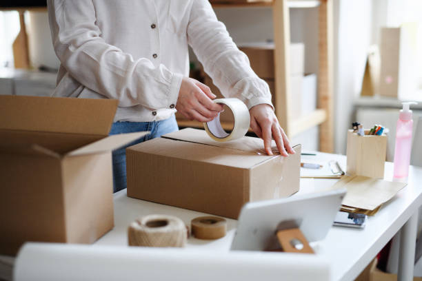 unrecognizable woman dropshipper working at home, packing parcels. coronavirus concept. - packaging packing adhesive tape box imagens e fotografias de stock