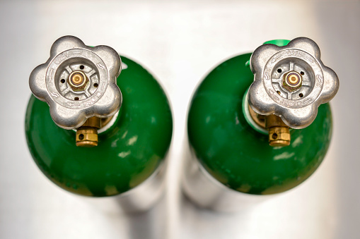 Looking down at two medical oxygen cylinders standing upright on stainless steel background.