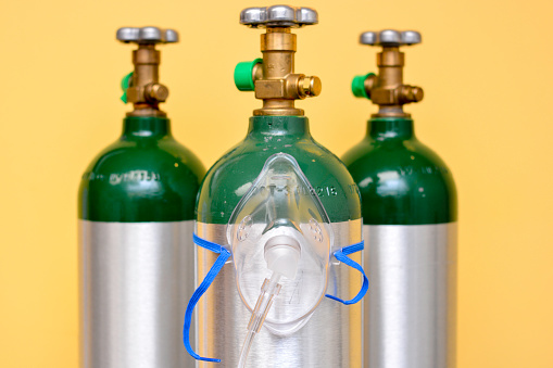 3 medical oxygen tanks on yellow background with oxygen mask on the center cylinder.