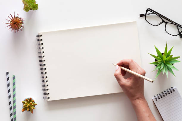 A white desk with an open sketchbook and a woman's hand. Drawing.