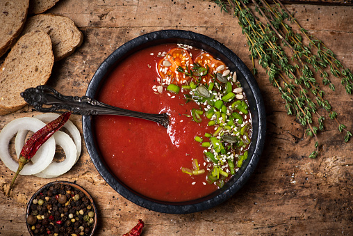 Tomato soup on a plate served on rustic wooden table with bread and food ingredients top view