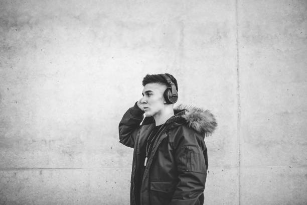 Young man in jacket listen music with headphones, posing over concrete background. Young man in jacket listen music with headphones, posing over concrete background.Black and white version. black and white headphones stock pictures, royalty-free photos & images
