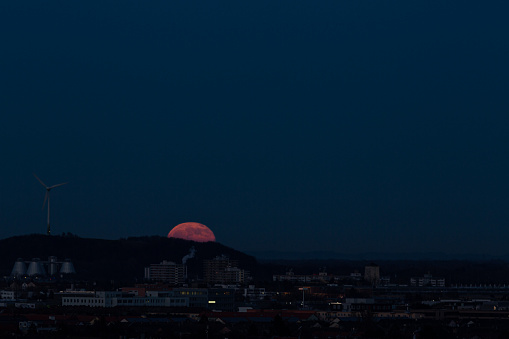 Big red full moon begins to rise over the horizon of the city