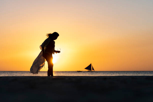 (foco seletivo) vista deslumbrante da silhueta de uma garota caminhando em uma praia durante um belo e romântico pôr do sol. white beach, ilha boracay, filipinas. - filipino ethnicity women philippines palawan - fotografias e filmes do acervo