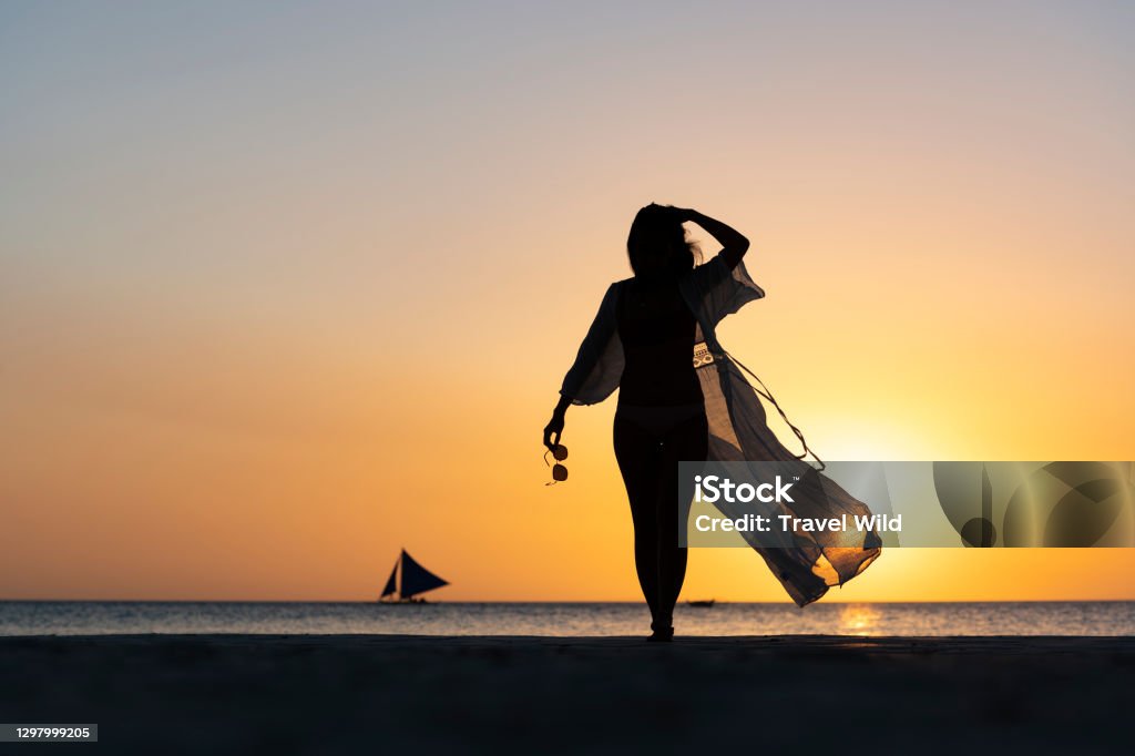 (Selective focus) Stunning view of the silhouette of a girl walking on a beach during a beautiful and romantic sunset. White Beach, Boracay Island, Philippines. Fashion Model Stock Photo