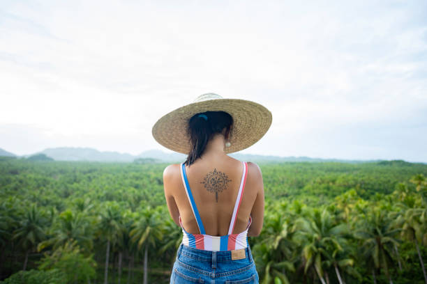 (Selective focus) Stunning view of a girl with a large straw hat admiring the palm tree forest is Siargao, Philippines. (Selective focus) Stunning view of a girl with a large straw hat admiring the palm tree forest is Siargao, Philippines. Siargao is a tear-drop shaped island in the Philippine Sea. summer fashion philippines palawan stock pictures, royalty-free photos & images