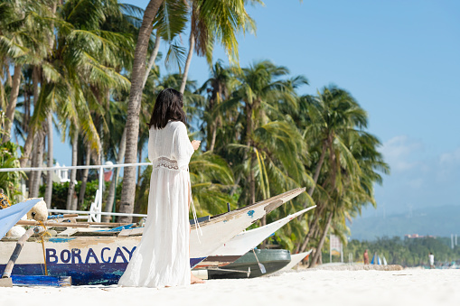 (Selective focus) Stunning view of a girl dressed in white, walking on a beach during a beautiful sunny day. White Beach, Boracay Island, Philippines.