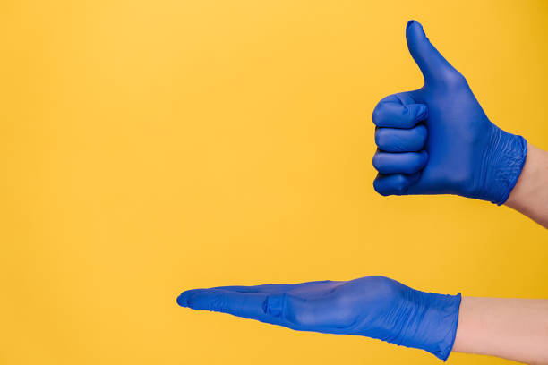 istock Unrecognizable young male opening palm and makes thumb up gesture, demonstrates approval or agreement, wears medical protective gloves, isolated on yellow wall for advertisement. Body language concept 1298005266