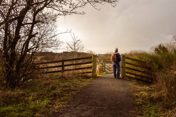 A retired man walking alone on a footpath in the countryside of Dumfries and Galloway south west Scotland he is dressed for the cold weather and is wearing a backpack