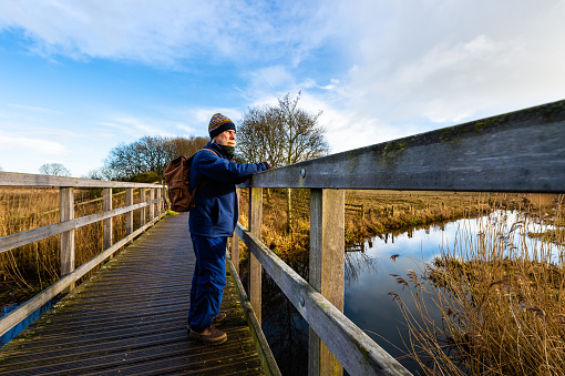 A retired man standing alone on a bridge in the countryside of Dumfries and Galloway south west Scotland he is dressed for the cold weather and is wearing a backpack