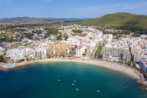 Aerial drone photo of the beautiful island of Ibiza in Spain showing the costal front golden sandy beaches with people relaxing and sunbathing on a hot sunny summers day