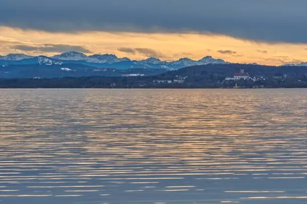 Reflecting lake during sunset with a mountain range in the background. Ammersee lake in Bavaria, Germany in the sunset.
