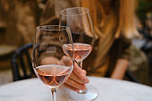 A glass of rose wine in the hands of a girl relaxing on restaurant terrace. Summer holiday. Celebrate and enjoy moment. Alcoholic drink tasting. Romantic evening aperitif. Wine glass closeup