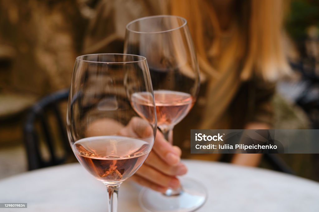 A glass of rose wine in the hands of a girl relaxing on restaurant terrace. Summer holiday. Celebrate and enjoy moment. Alcoholic drink tasting. Romantic evening aperitif. Wine glass closeup Wine Stock Photo