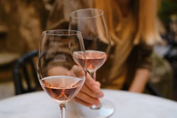 A glass of rose wine in the hands of a girl relaxing on restaurant terrace. Summer holiday. Celebrate and enjoy moment. Alcoholic drink tasting. Romantic evening aperitif. Wine glass closeup