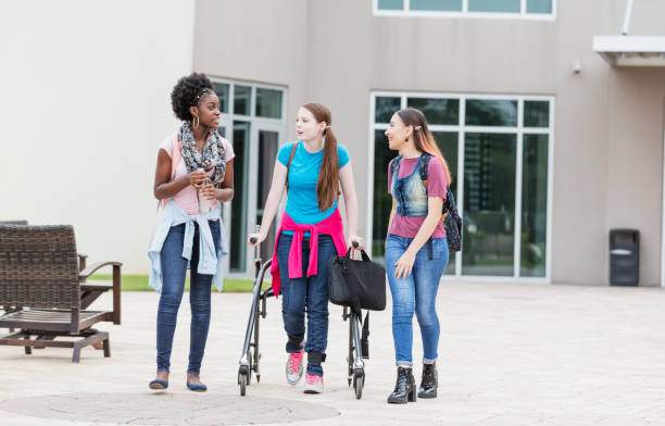 Multi-ethnic high school girls walking and talking A multi-ethnic group of three teenage girls conversing as they walk outside their high school building. The girl in the middle is using a walker. Her friends are African-American and  Hispanic. teenagers only teenager multi ethnic group student stock pictures, royalty-free photos & images