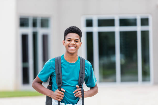 African-American teenager standing outside school An African-American teenage boy, 15 years old, standing outside a school building, smiling at the camera. He is a high school student. young black boys stock pictures, royalty-free photos & images