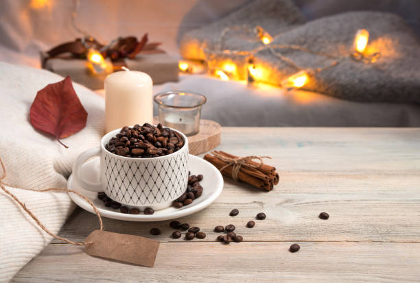 Evening coffee background with whole coffee beans in a mug, candle and sweater on the background of burning lights
