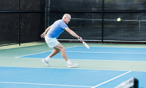 Mature man playing pickleball A mature man in his 50s playing pickleball. He is on an outdoor court, getting ready to hit the ball which is in mid-air. paddle ball stock pictures, royalty-free photos & images