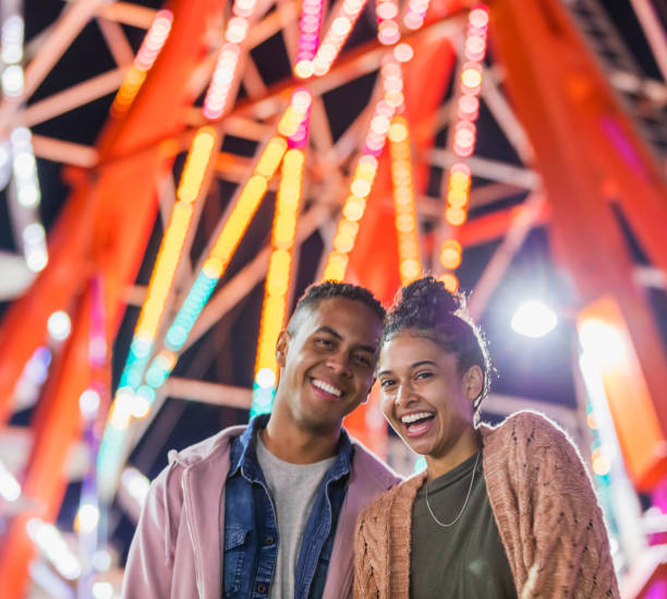 istock Young couple at county fair, by ferris wheel 1298023600