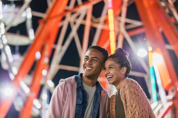 istock Young couple at county fair, by ferris wheel 1298023611
