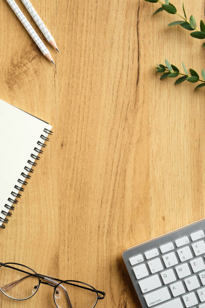 istock Feminine workspace top view. Flat lay keyboard, paper notebook, pencils, glasses, eucalyptus leaves on wooden table. Modern home office desk, overhead 1298026159