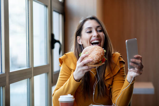 Young lady is eating burger, posing, taking selfie.
