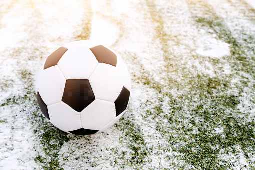 Soccer ball placed on snowy grass in winter on sports ground, copy space
