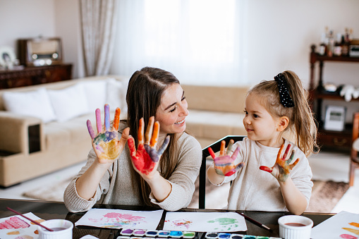 Mother reaching her daughter how to paint on canvas