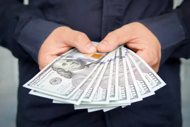Photo of male hands with wrist watch is considered American dollars. Hands holding dollar cash. 1000 dollars in 100 bills in a man hand close-up on a dark background. hundred