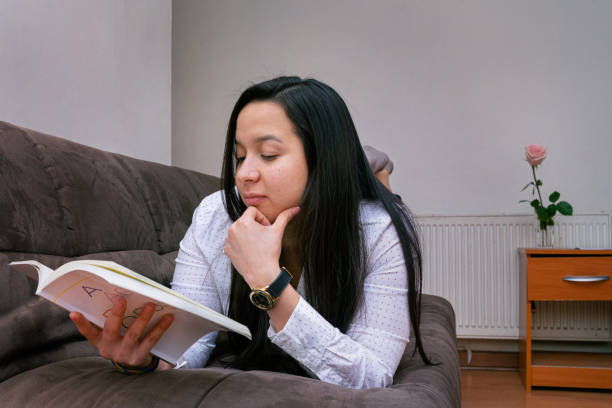 istock Young latin woman laying on a sofa reading a book 1298031523