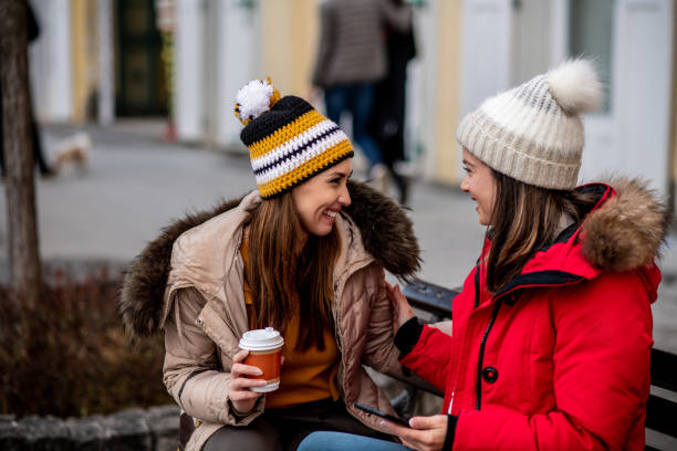 istock Two lovely ladies are sitting on bench, drinking coffee and talking. 1298032371