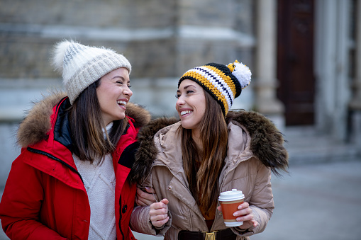 A young woman is talking with her friend, drinking coffee and walking around the city. Both of them have most wonderful time, since they haven't seen each other for long time.