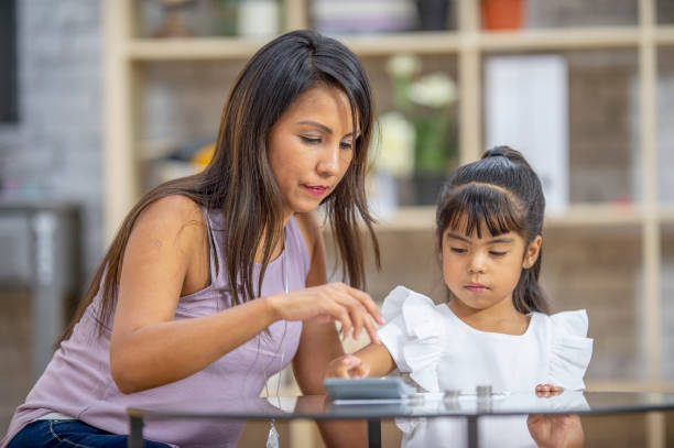 Let's count our coins together A mother and daughter are sitting at a table in their living room. They are counting her daughter's piggybank coins together. There is a calculator on the table. financial literacy stock pictures, royalty-free photos & images