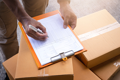 Warehouse worker writing paper on clipboard. inventory management of product. Checking stock. parcel shipment boxes.