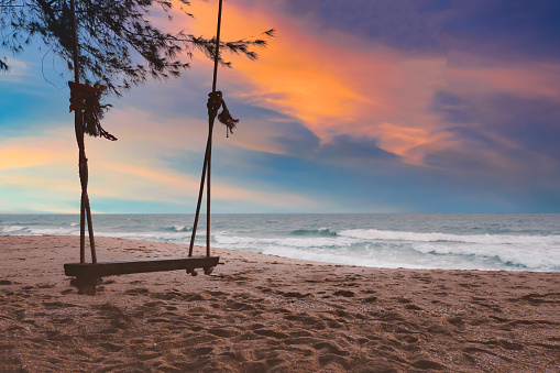 Silhouette Wooden swing on the beach at sunset on colorful sky background.