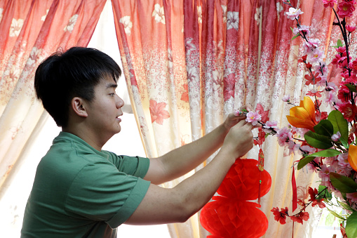 An Asian young man is decorating red lanterns at residence to welcome Lunar New Year.