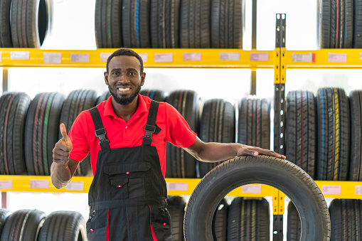 Smiling African mechanic with a tire over garage tires shop background