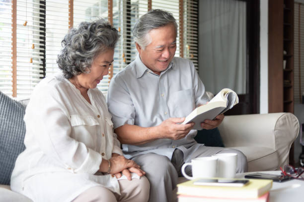 自宅で一緒に本を読んでソファに座って恋に幸せなアジアのシニアカップル。 - senior adult relaxation sofa reading ストックフォトと画像