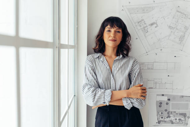 Confident female architect standing in office Portrait of female architect standing beside architecture drawings in office. Businesswoman standing in office with arms crossed. architect stock pictures, royalty-free photos & images